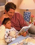 Bilde av far lytter til sin sønn lese en bok ved sengetid