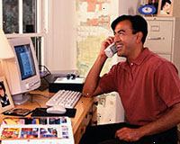 Bilde av en mann som jobber på datamaskinen, snakker i telefonen