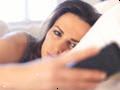 Ulykkelig kvinne i sengen å se på hennes mobiltelefon